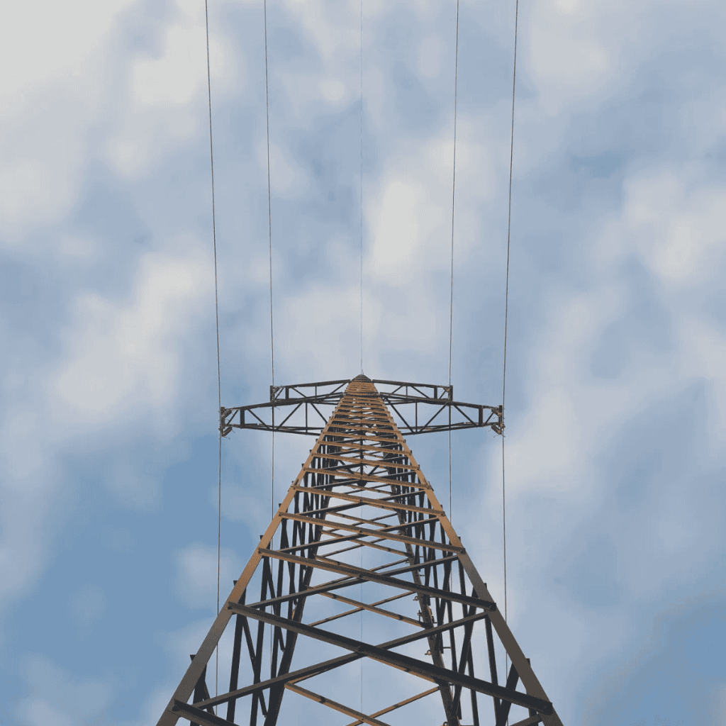Een hoge metalen hoogspanningsmast met elektriciteitskabels tegen een lichtbewolkte blauwe lucht.